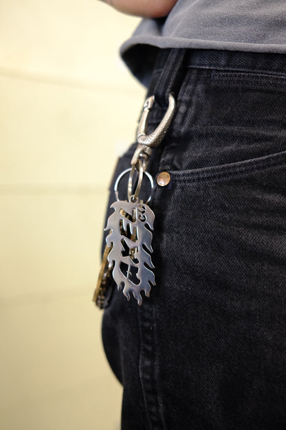 Metal keychain with a flame design attached to a belt loop of jeans