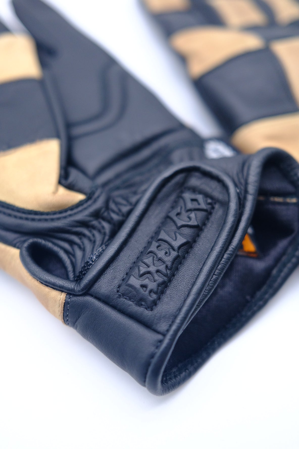 Close-up of a black and beige glove with a Axel logo embossed on the wrist strap