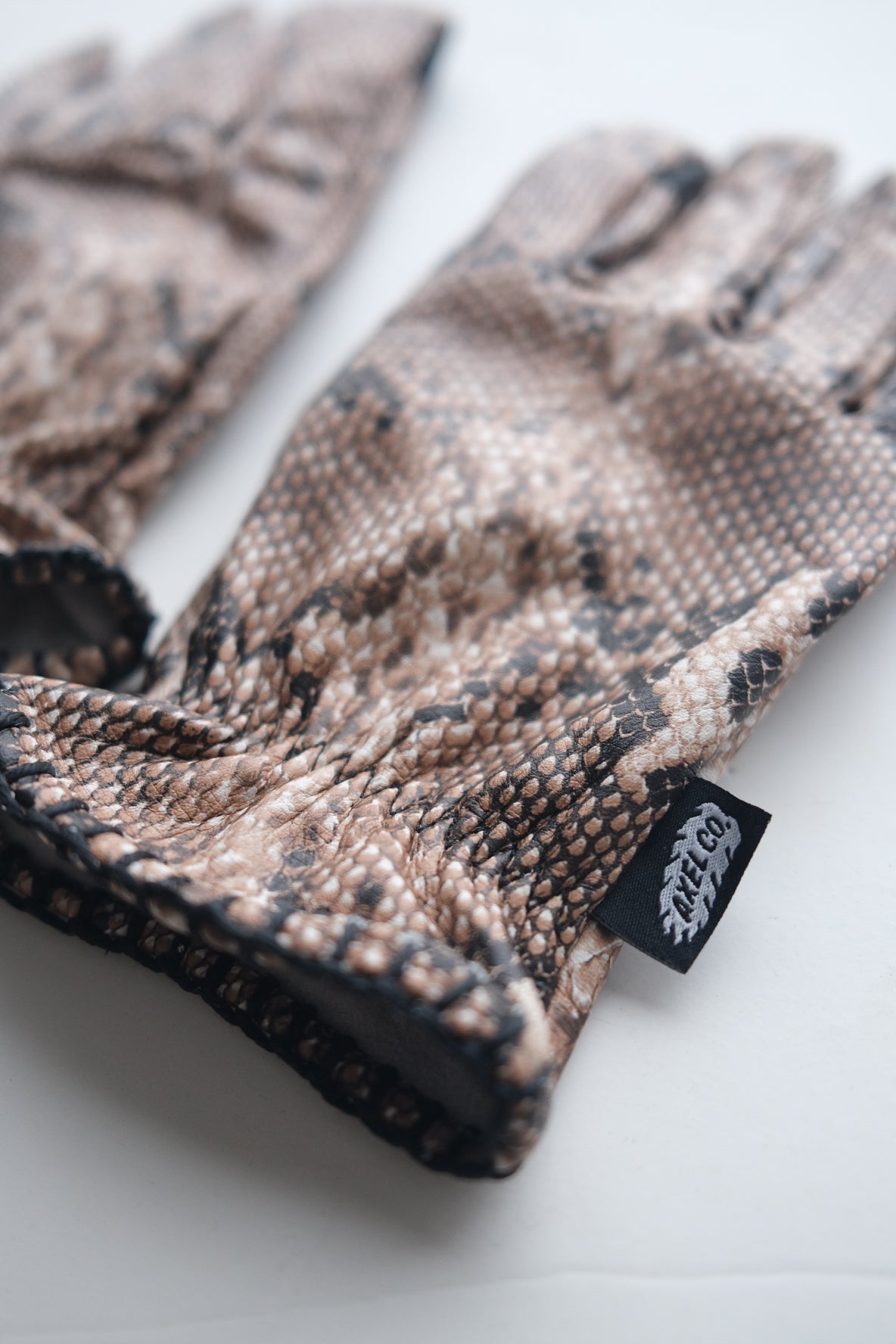 Snake skin patterned glove with a Axel Co tag on a white background